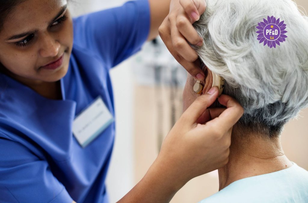 An audiologist assisting an older person with a hearing aid